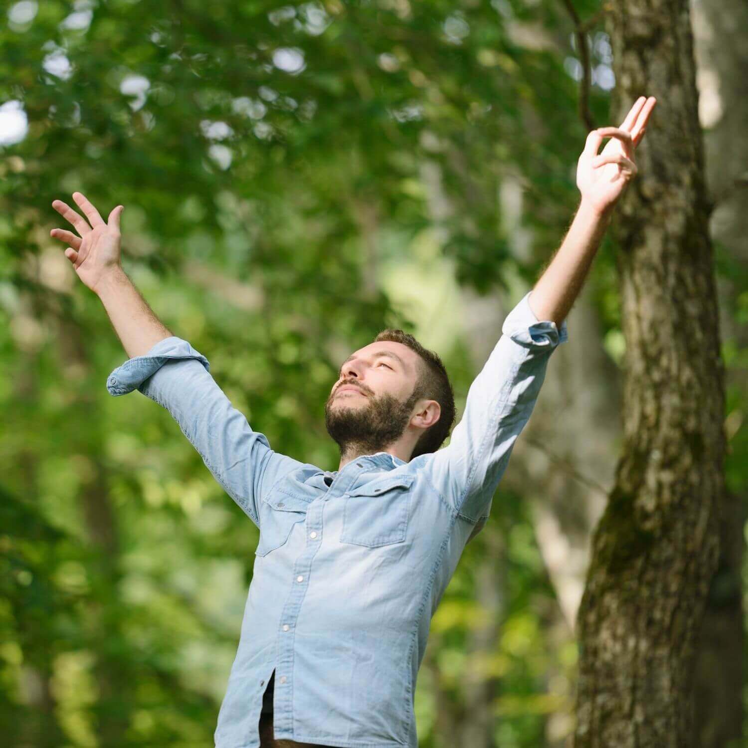 Homme exprimant la joie en plein air, entouré par la nature, avec les bras levés vers le ciel.