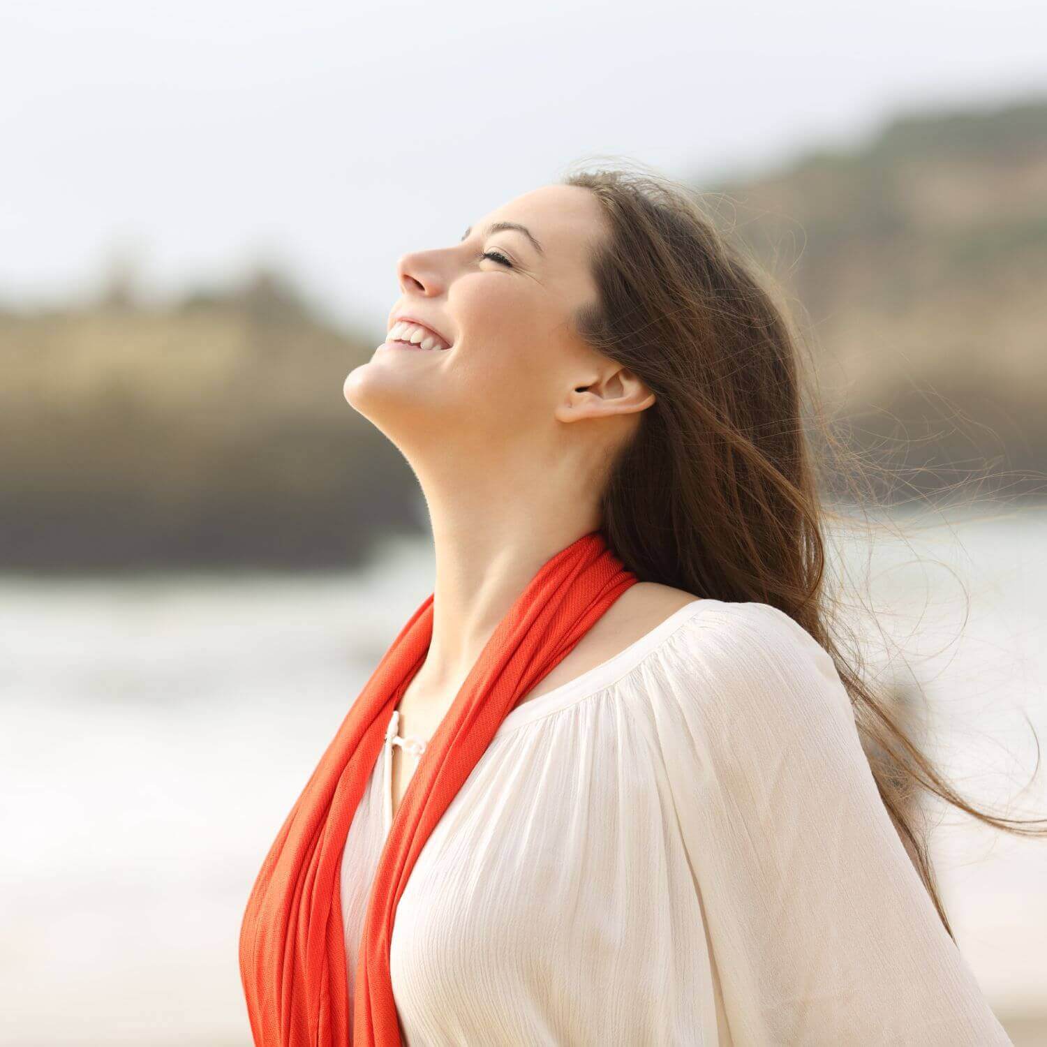 Femme souriante à la plage avec un foulard rouge, illustrant le bonheur et la sérénité.