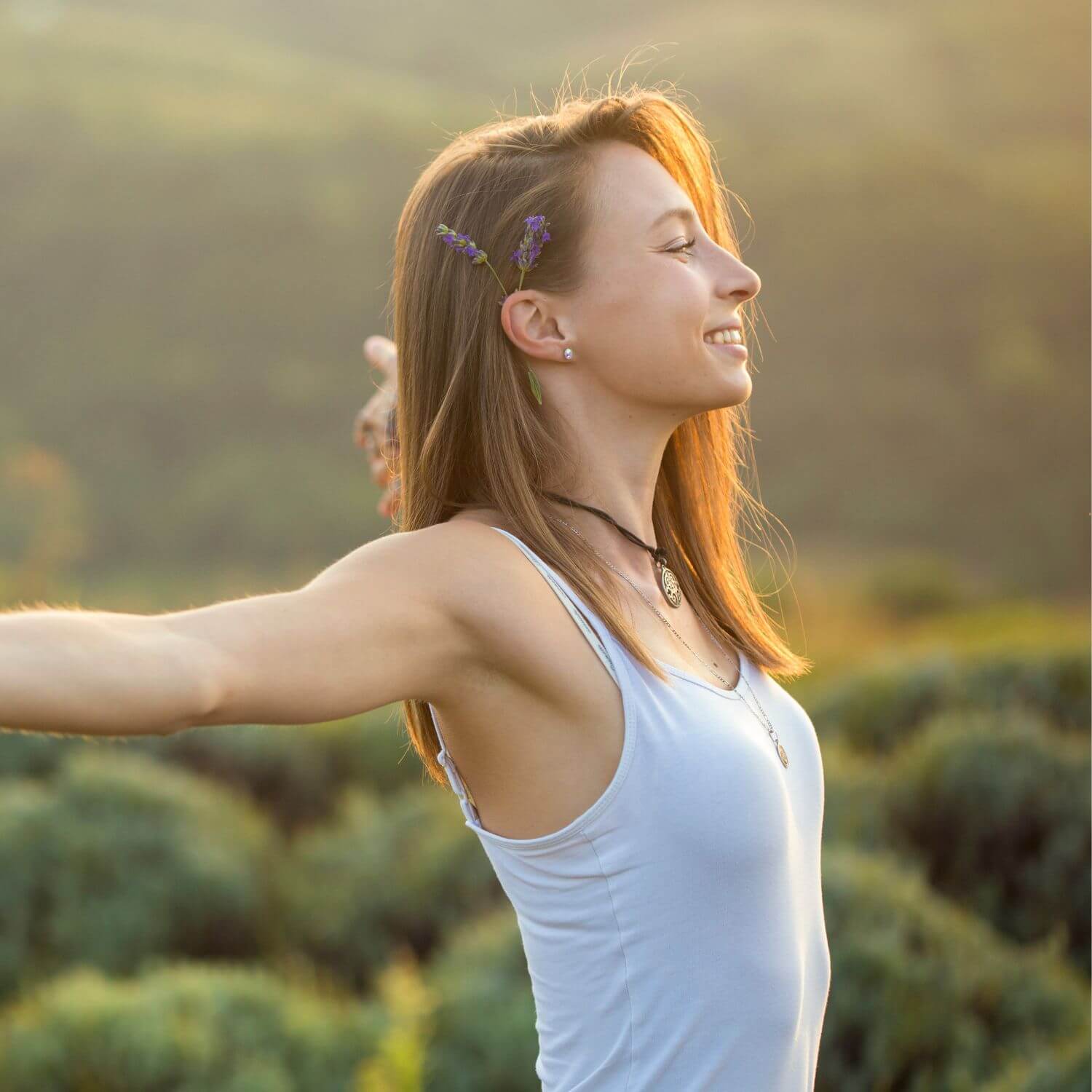 Femme souriante dans un paysage naturel, esprit libre et apaisé, évoquant bien-être et sérénité.