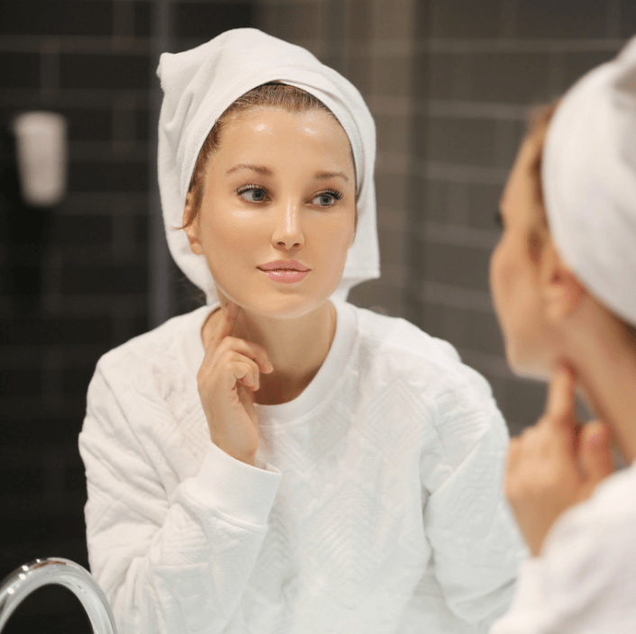 Femme utilisant le Spray de Réparation Ultime pour une peau douce et éclatante dans le miroir.
