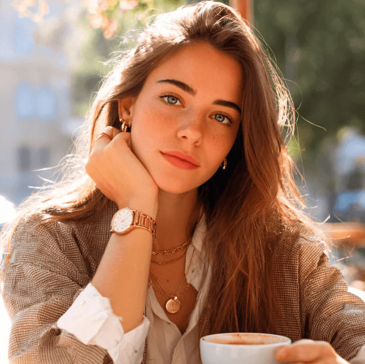 Jeune femme avec un café, portant des bijoux et une montre, exprimant un style de vie élégant.