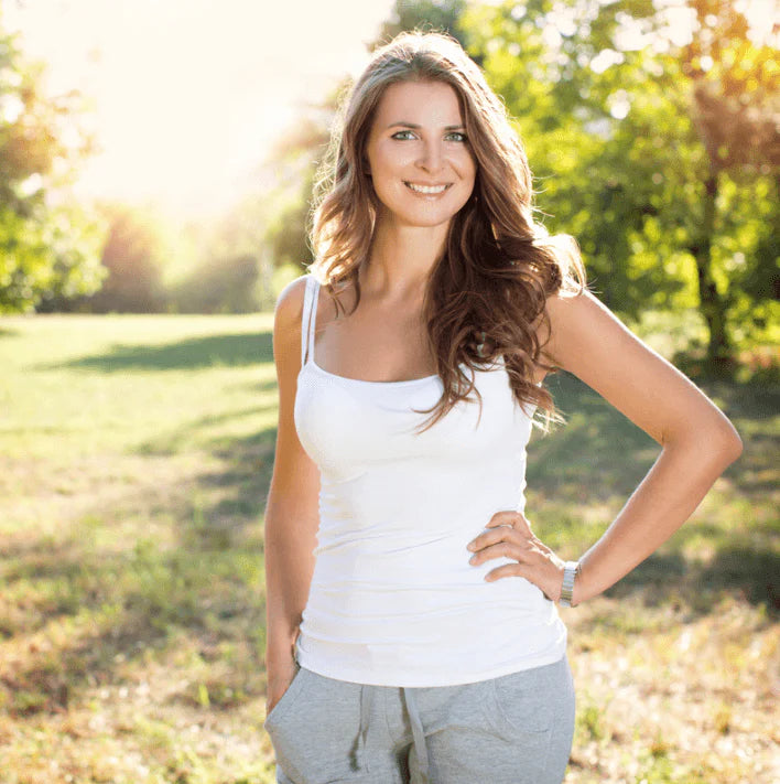 Huile Vital Ease applied by a smiling woman in a sunlit park, showcasing healthy skin and radiance.