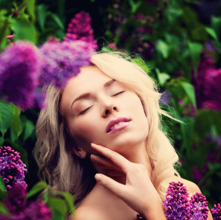 Femme souriante entourée de fleurs lilas, mettant en valeur la beauté naturelle et l'éclat de la peau.
