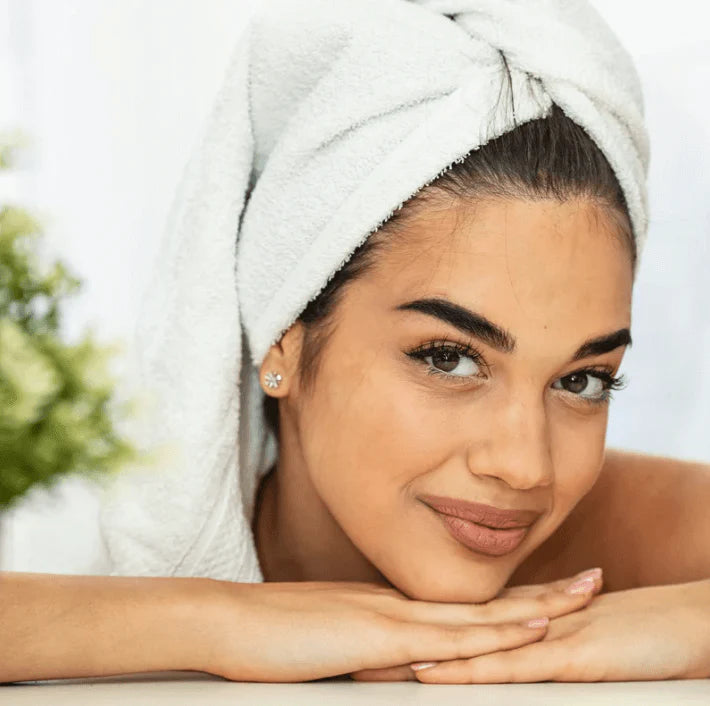 Femme avec serviette sur la tête, affichant un sourire radieux après un soin, idéale pour promouvoir le Sérum liftant.