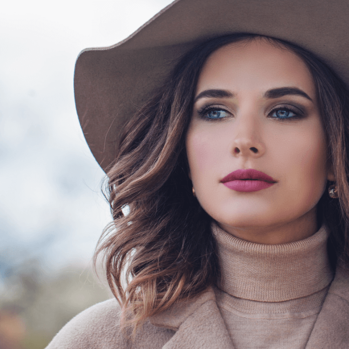 Huile essentielle de soin des lèvres sur des lèvres éclatantes d'une femme en chapeau.
