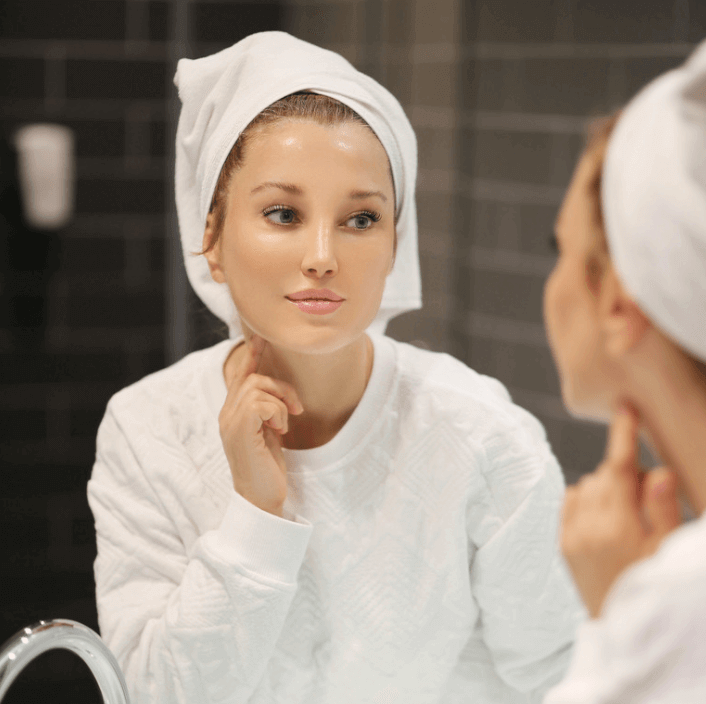 Femme utilisant Baume Contour des Yeux Luxe tout en se regardant dans le miroir.