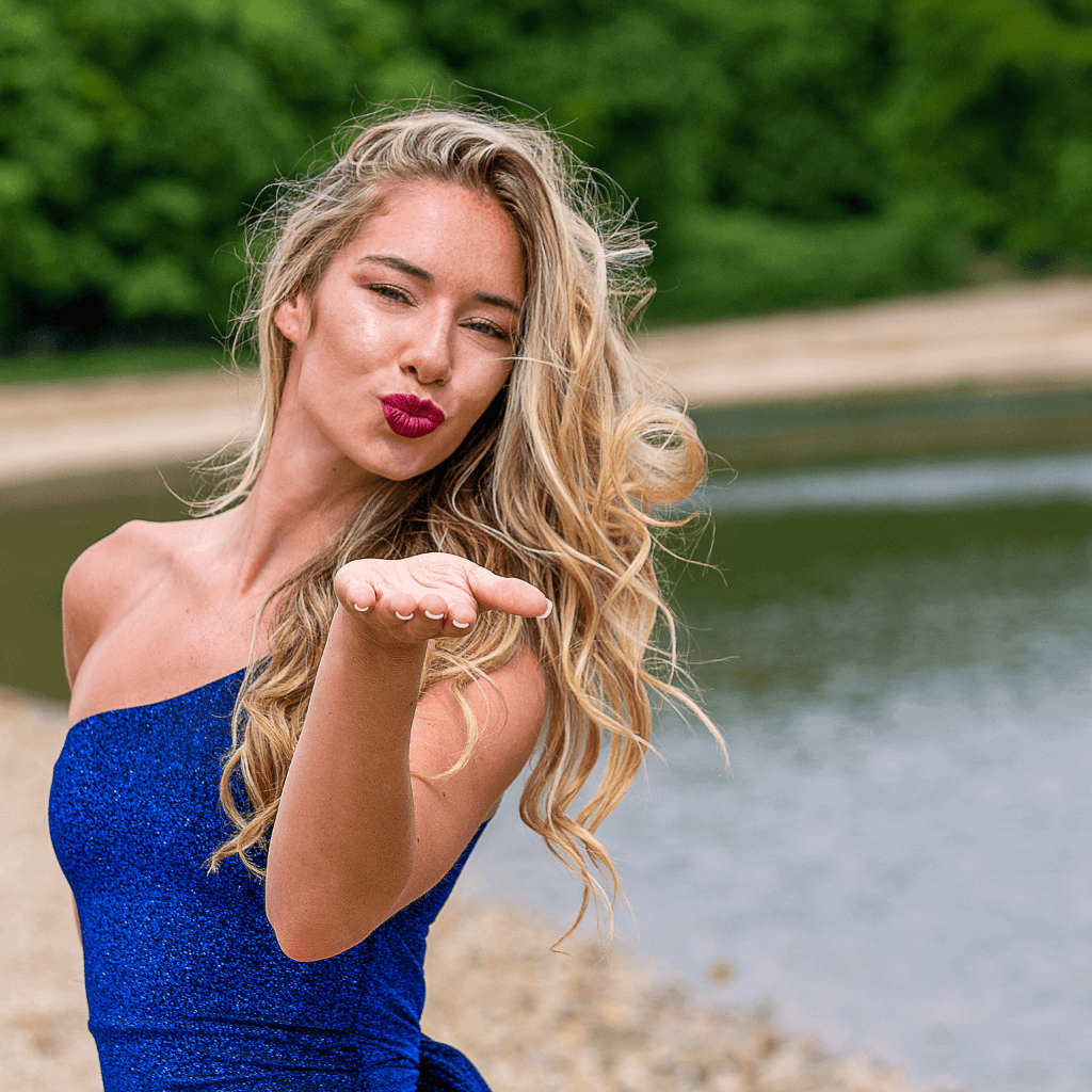Femme avec des cheveux blonds et une robe bleue, envoyant un baiser près d'un plan d'eau en plein air.