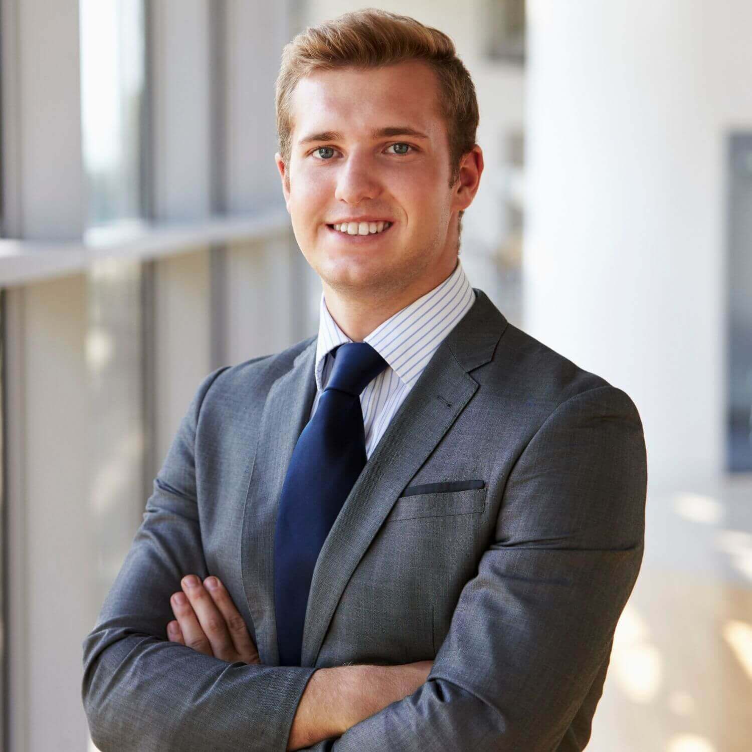 Homme en costume, souriant, avec les bras croisés dans un environnement moderne.