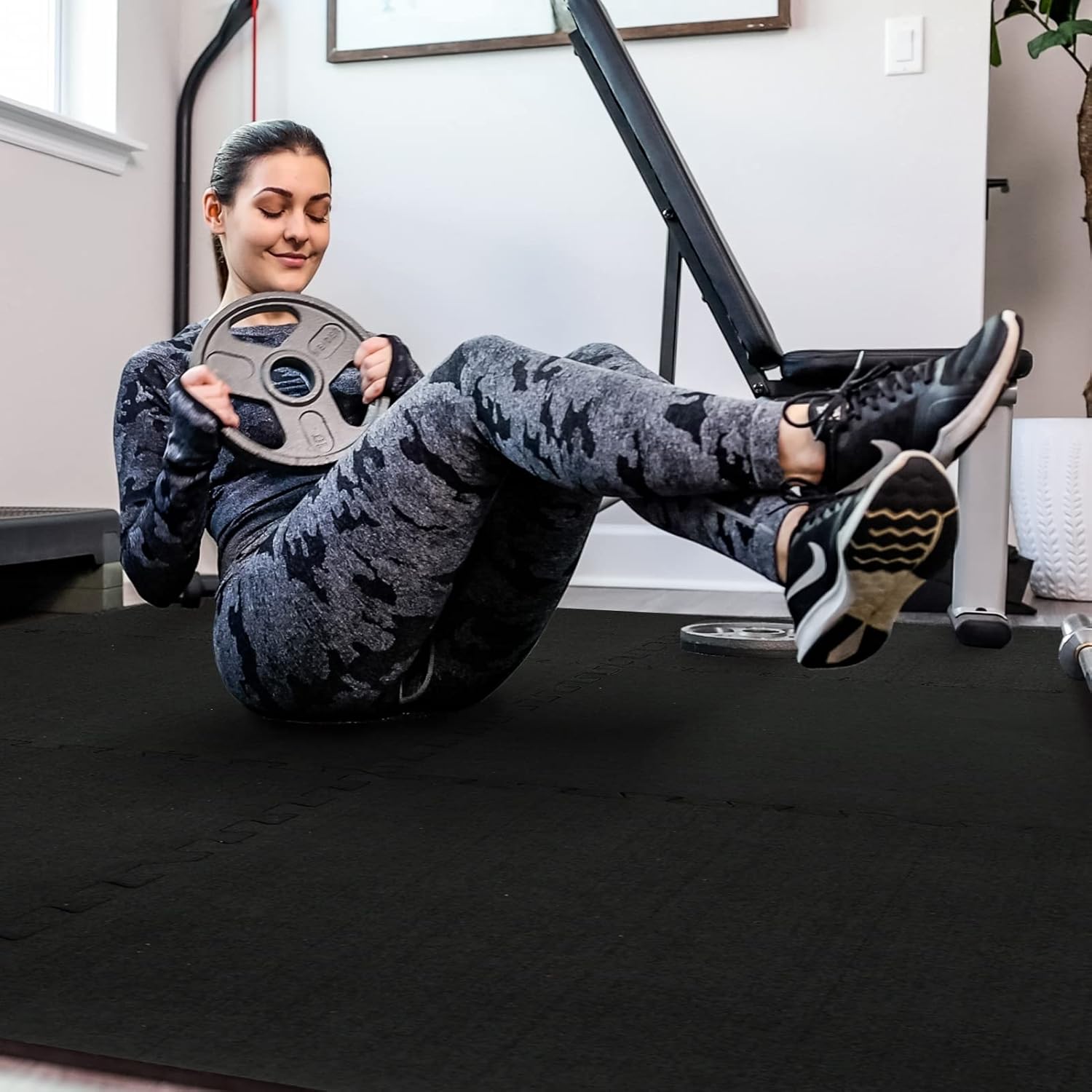Woman exercising on a mat, using a weight plate for abdominal workouts in a modern gym setting.