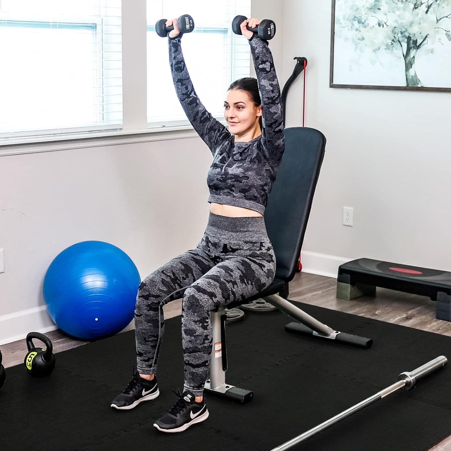Woman in workout gear performing overhead dumbbell press in gym setting.