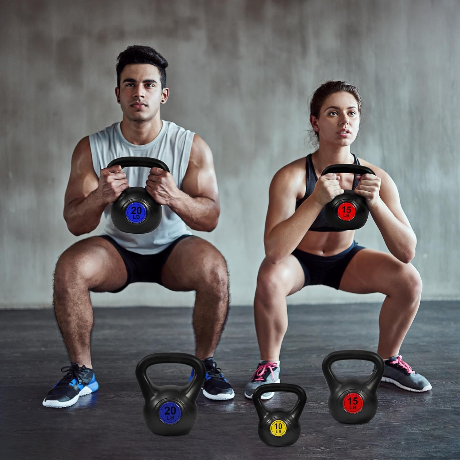 Un homme et une femme s'entraînant avec l'Autera CoreBell™ lors d'un squat, entourés de kettlebells de différentes tailles.