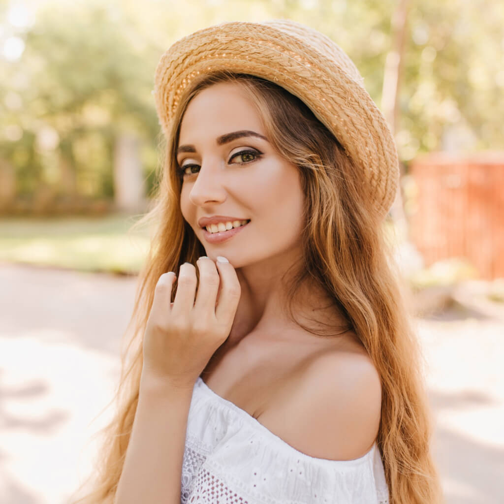 Femme souriante avec un chapeau de paille dans un cadre naturel ensoleillé.