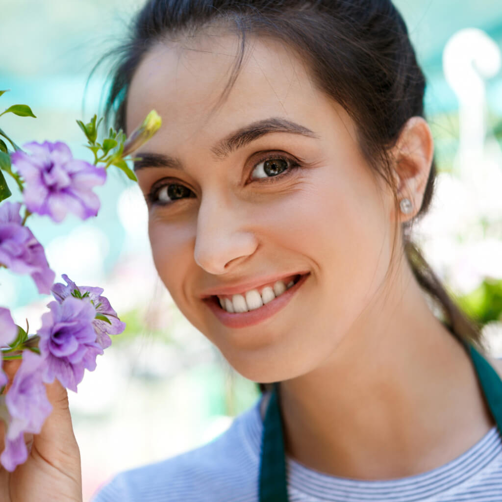 Femme souriante tenant des fleurs violettes, représentant une ambiance joyeuse de jardinage.